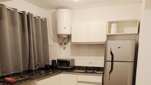 Eine kompakte Küche mit weißen Schränken, einem Edelstahl-Kühlschrank, einer Mikrowelle und einem kleinen Topfpflanzen auf der Arbeitsplatte.