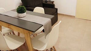 Ein kleiner, moderner Raum mit Esstisch, Stühlen, einer Couch, einer Lampe und einem Telefon an der Wand.