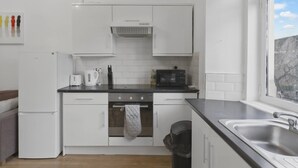 Una cucina moderna con mobili bianchi, un piano di lavoro nero, forno integrato, microonde e una finestra vista su un paesaggio roccioso.