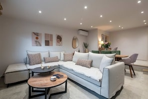 A modern living room with a sectional sofa, a round coffee table, and a dining area with a table and chairs.