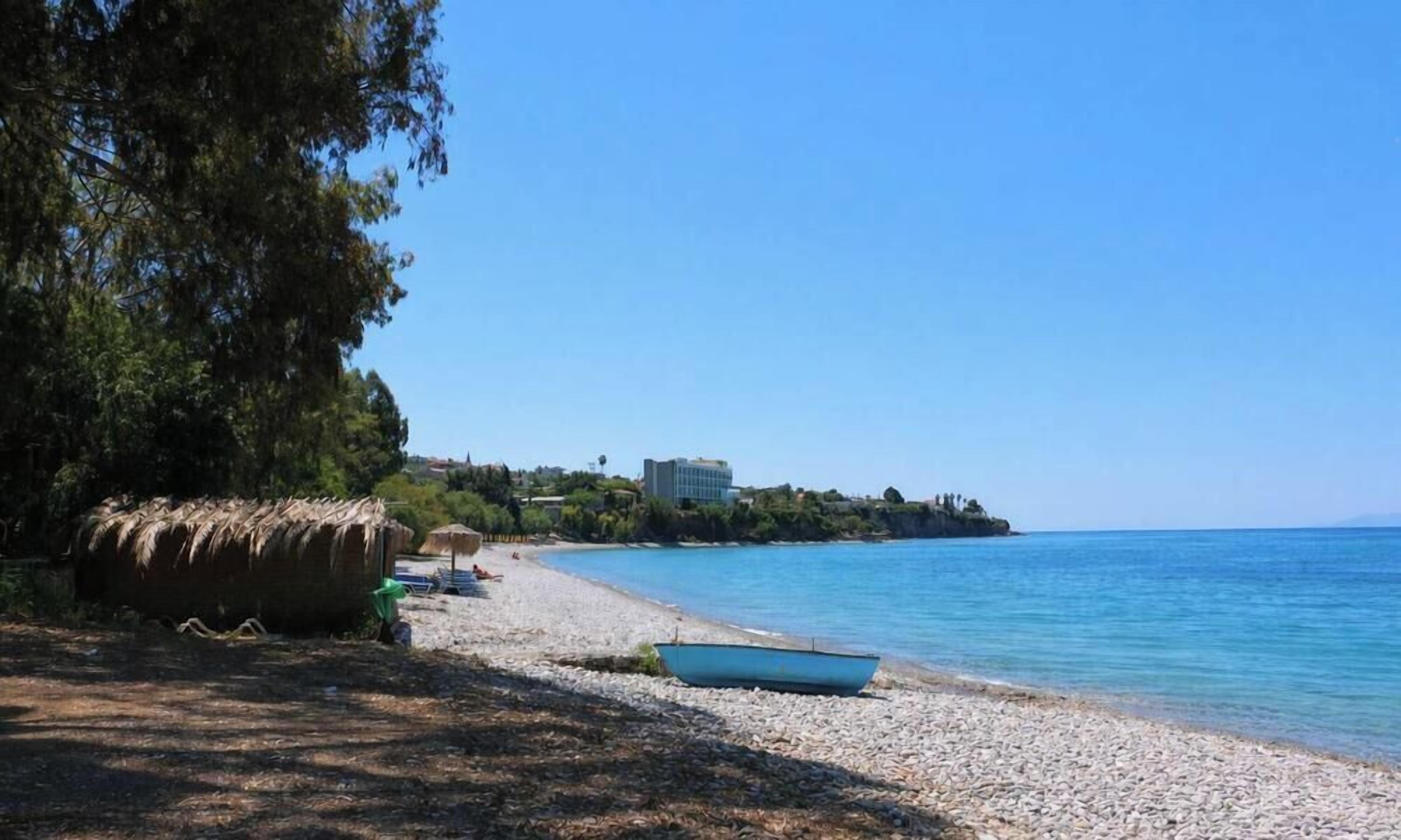 A beach with pebbles, a boat, and a building in the background.