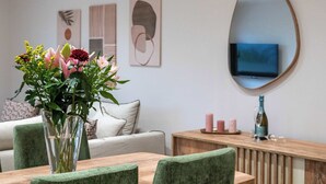 Un comedor con una mesa, sillas, un florero con flores, un espejo y obras de arte en la pared.