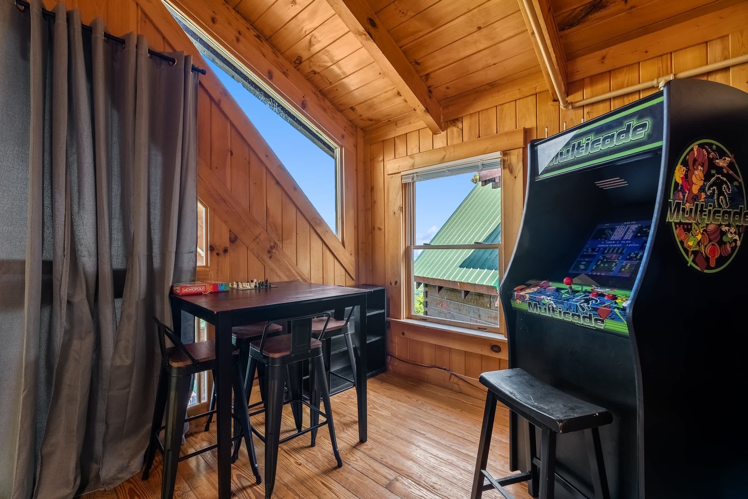 A wooden room with a table, chairs, a game console, and a window.