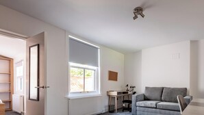 Ett rum med ett stort fönster, ett skrivbord, en grå soffa och en stol.