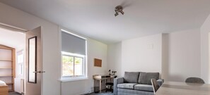 A room with a large window, a desk, a grey sofa, and a chair. - Marine Place | Flat 14 (St Andrews)