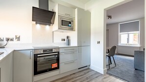 Ett modernt kök med inbyggda vitvaror, en matplats med en stol och utsikt över omgivningen genom ett fönster.