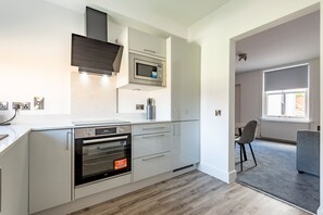 A modern kitchen with built-in appliances, a dining area with a chair, and a view of the outside through a window. - Marine Place | Flat 14 (St Andrews)