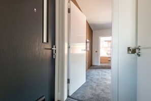 A hallway with a carpeted floor, a door with a handle, and a wooden panel wall. - Marine Place | Flat 14 (St Andrews)