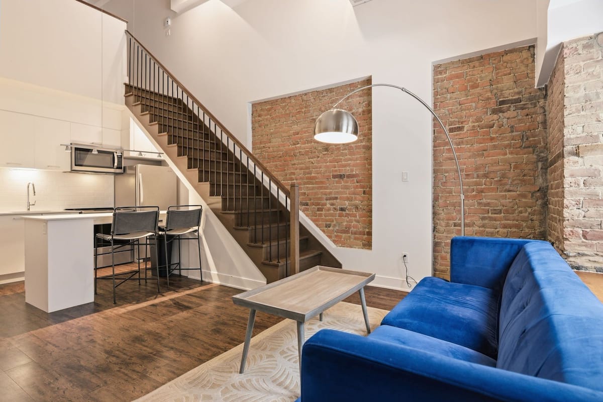 Una cocina moderna con microondas incorporado, un comedor con taburetes de bar, una escalera y un sofá azul en la sala de estar.