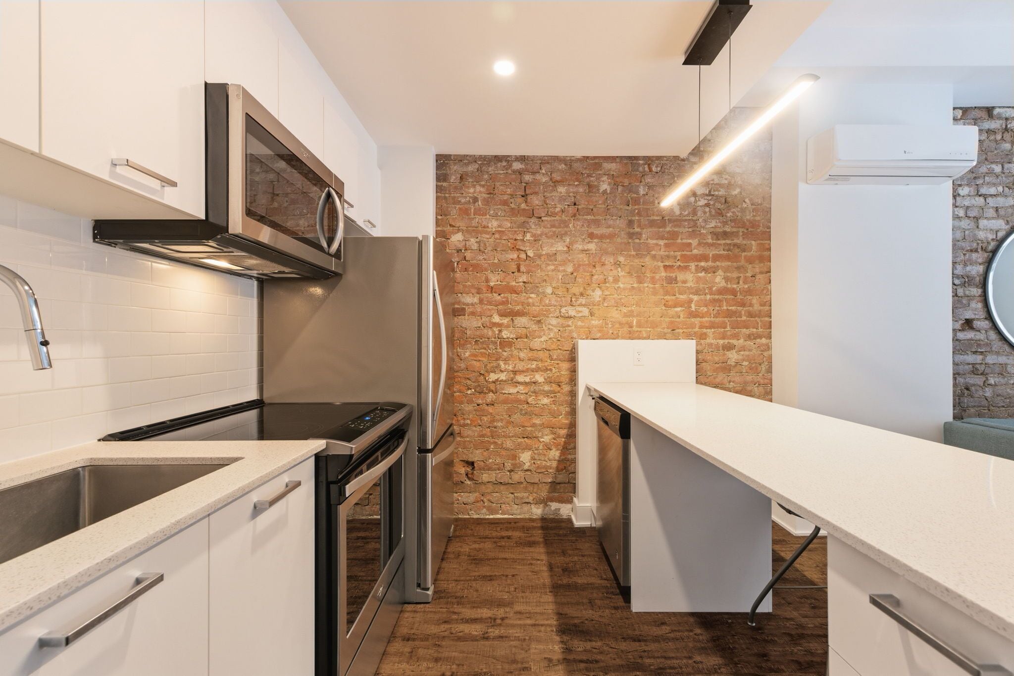 Una cucina moderna con mobili bianchi, una parete decorata in mattoni, elettrodomestici in acciaio inossidabile e un piano di lavoro lungo.