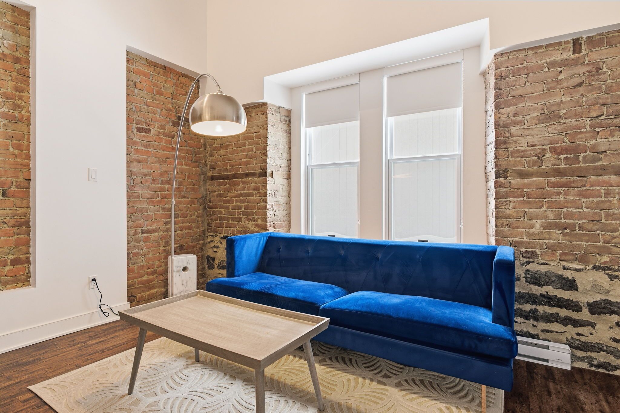 Une pièce avec un canapé bleu, une table basse en bois, une lampe suspendue et des murs en briques.