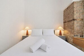 Ein Hotelzimmer mit einem ordentlich bezogenem Bett, zwei Nachttischlampen, einer Ziegelwand und einem hölzernen Nachttisch.