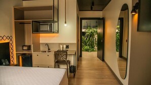 A modern hotel room with a bed, kitchenette, desk, and a view of a garden. - COROADOS HOTEL E FLATS LTDA (Nova Prata)
