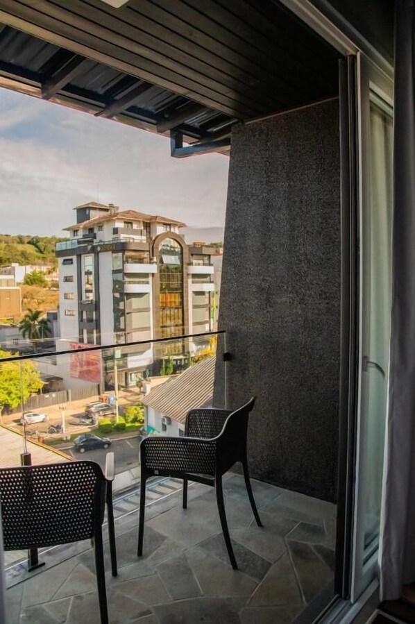 Un balcon avec deux chaises, une table en verre et une vue sur un immeuble moderne.