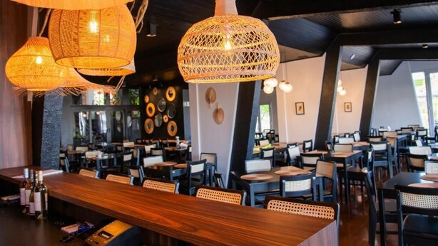 A restaurant with multiple tables and chairs, hanging wicker lamps, and a bar area with bottles. - COROADOS HOTEL E FLATS LTDA (Nova Prata)