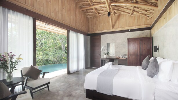 A bedroom with a large bed, a desk, a chair, and a view of greenery outside. - Babakan Hill Villas (Karangasem)