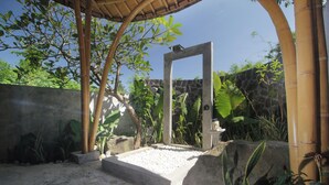 A concrete structure with a stone wall and bamboo elements in a garden setting. - Babakan Hill Villas (Karangasem)