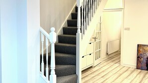 Una escalera con barandilla blanca, piso de madera y una puerta que da a otra habitación.