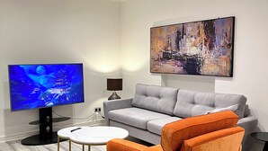 Una sala de estar moderna con un sofá gris, un sillón naranja, un televisor de pantalla plana, una mesa de centro redonda y un cuadro abstracto grande en la pared.
