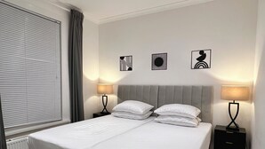 Una cama doble con cabecera gris, dos mesitas de noche con lámparas y tres obras de arte en la pared.