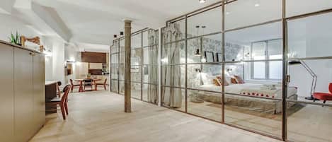 Un intérieur moderne avec une grande porte-fenêtre coulissante donnant sur une chambre, un coin repas avec des meubles en bois et une cuisine à l’arrière-plan.