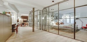 Un intérieur moderne avec une grande porte-fenêtre coulissante donnant sur une chambre, un coin repas avec des meubles en bois et une cuisine à l’arrière-plan.