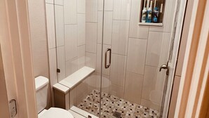 A shower with a glass door, a toilet, and a small shelf with toiletries.