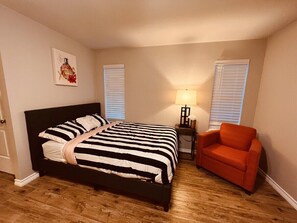 Une chambre à coucher comprenant un lit, une chaise, une table de chevet et une lampe fixée au mur.