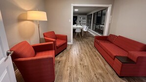 A compact living space with a red sofa, matching armchairs, a floor lamp, and a dining area in the background.