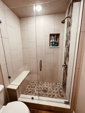 Une douche avec une porte en verre, une étagère pour les articles de toilette et un sol carrelé.