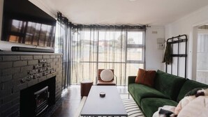 A living room with a fireplace, a green sofa, a coffee table, and a view through large windows. - Derwent River Holiday Home - Minutes to Hobart (Midway Point)