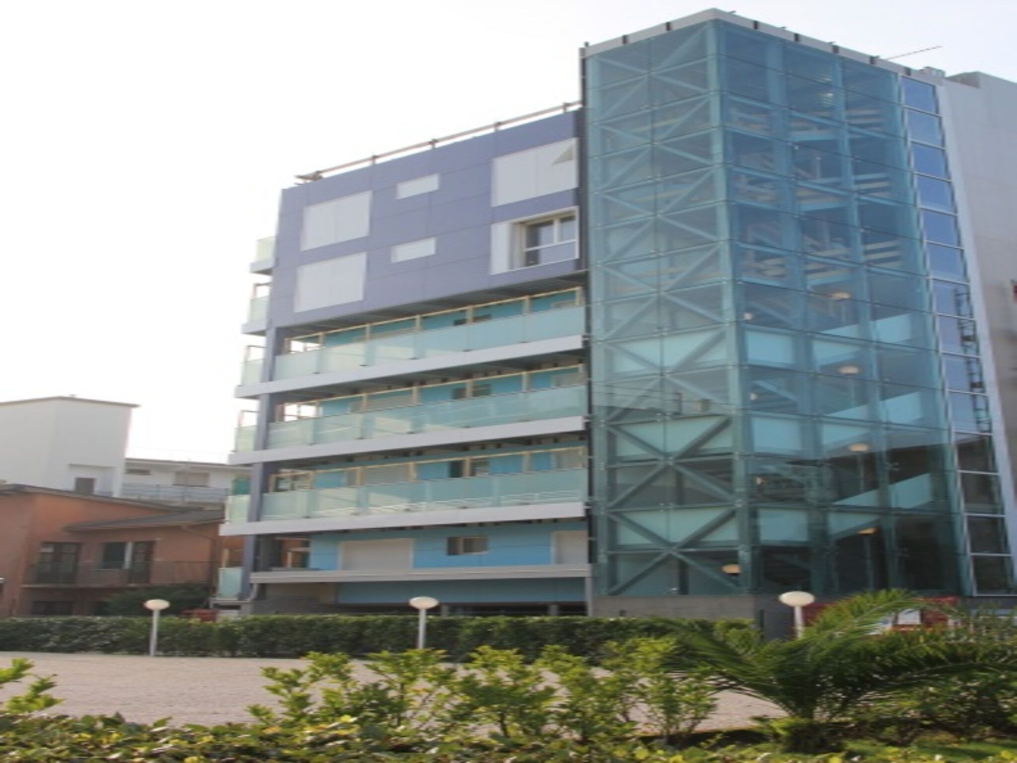 Un edificio a più piani con facciata in vetro, balconi e un cortile con piante.