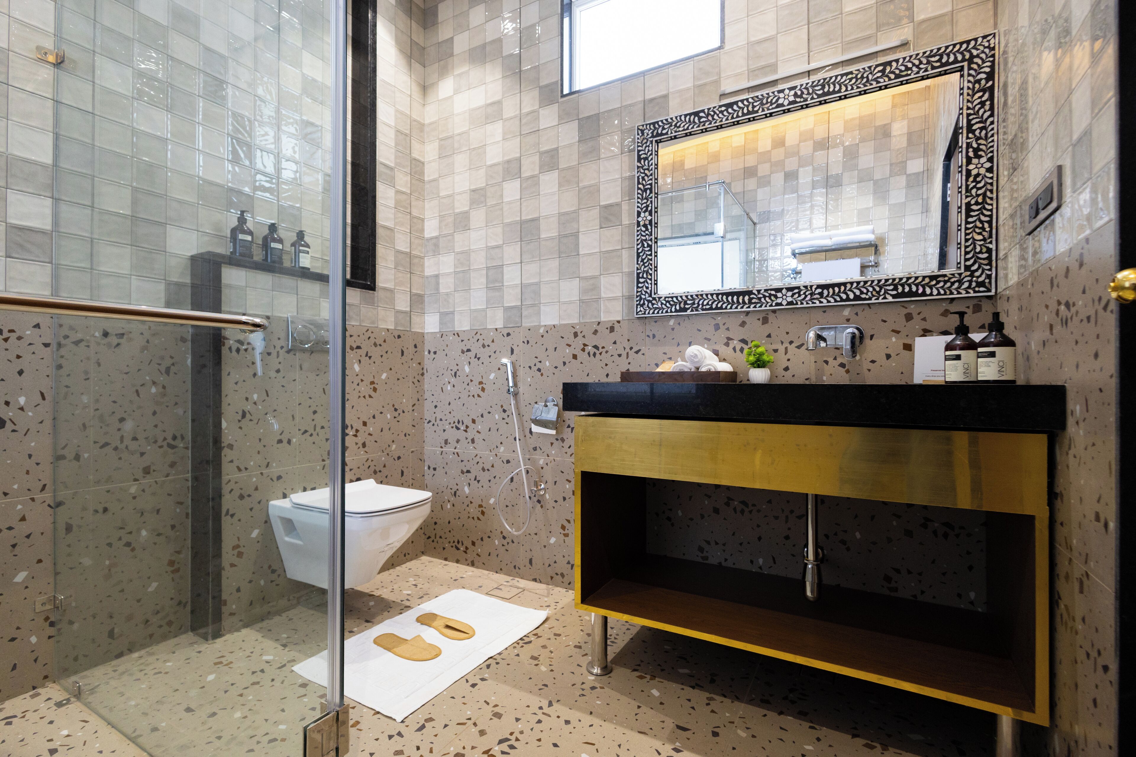 A modern bathroom with a glass shower enclosure, a white toilet, a black and gold vanity, and a large mirror with a decorative frame.