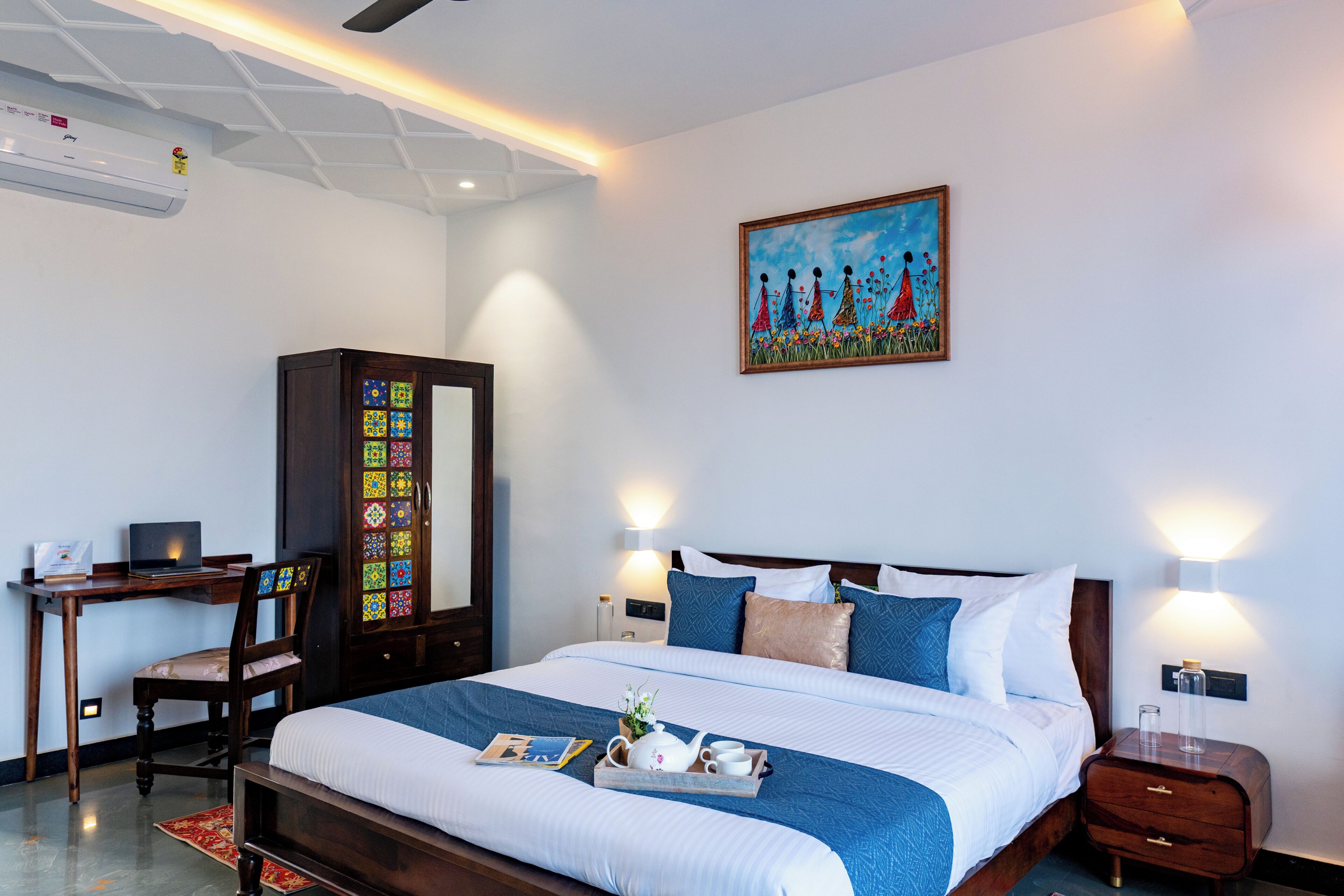 A hotel room with a bed, desk, chair, and artwork on the wall.
