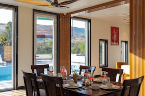 A dining area with a table set for four, large windows with a view of the outdoors, and a ceiling fan.