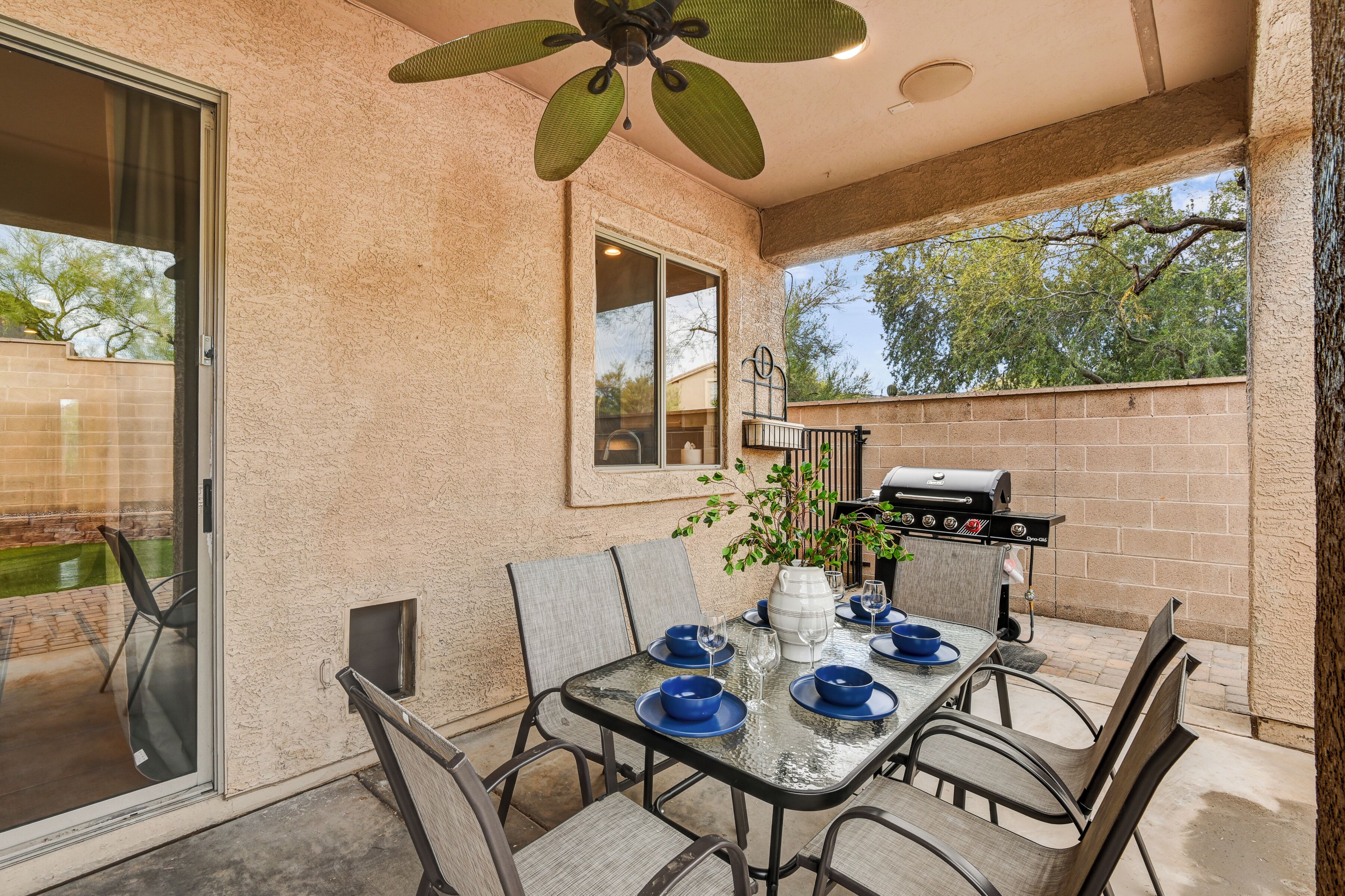 Une terrasse extérieure avec une table dressée pour les repas, un barbecue et un ventilateur de plafond.