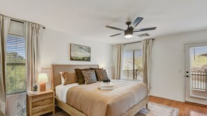 Un dormitorio con cama, mesita de noche, lámpara, ventilador de techo y un cuadro en la pared.