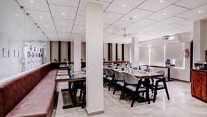 A modern dining area with a long bench, multiple tables, and chairs. - Classic The Grand Unity (Garudeshwar)