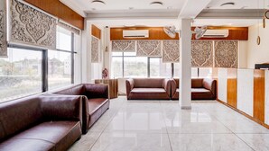 A spacious lobby with leather sofas, large windows, and decorative wall panels. - Classic The Grand Unity (Garudeshwar)