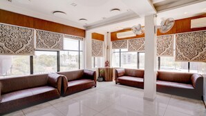 A spacious lobby with two leather sofas, large windows, decorative wall panels, and ceiling fans. - Classic The Grand Unity (Garudeshwar)