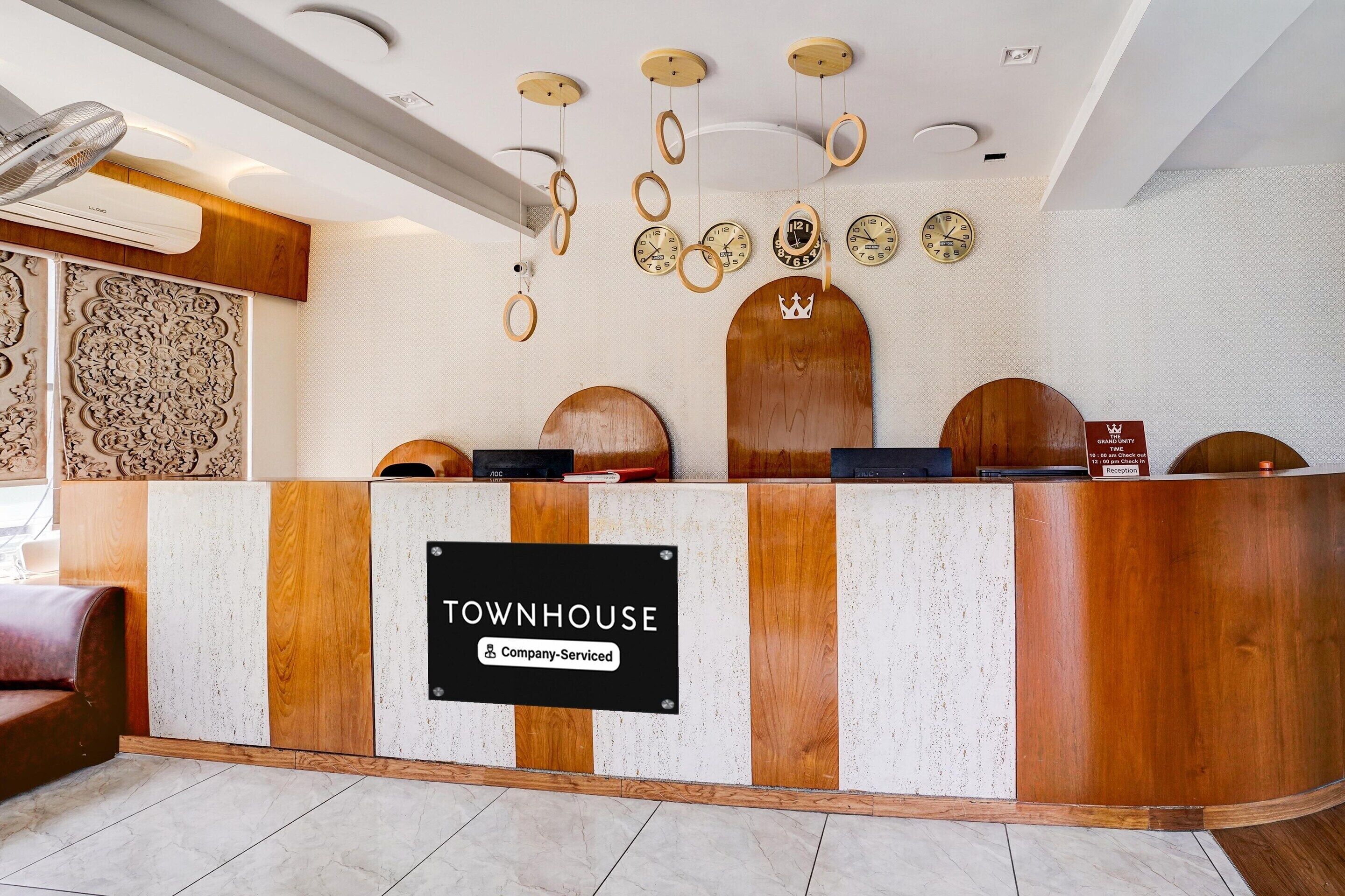 A reception desk with a sign reading 'TOWNHOUSE Company-Serviced,' wooden wall panels, a ceiling fan, and decorative wall clocks.