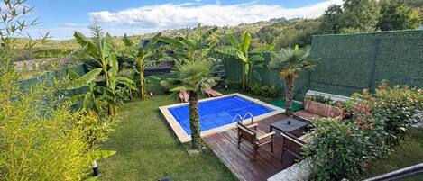 A backyard with a swimming pool, a barbecue grill, and a patio with outdoor furniture.