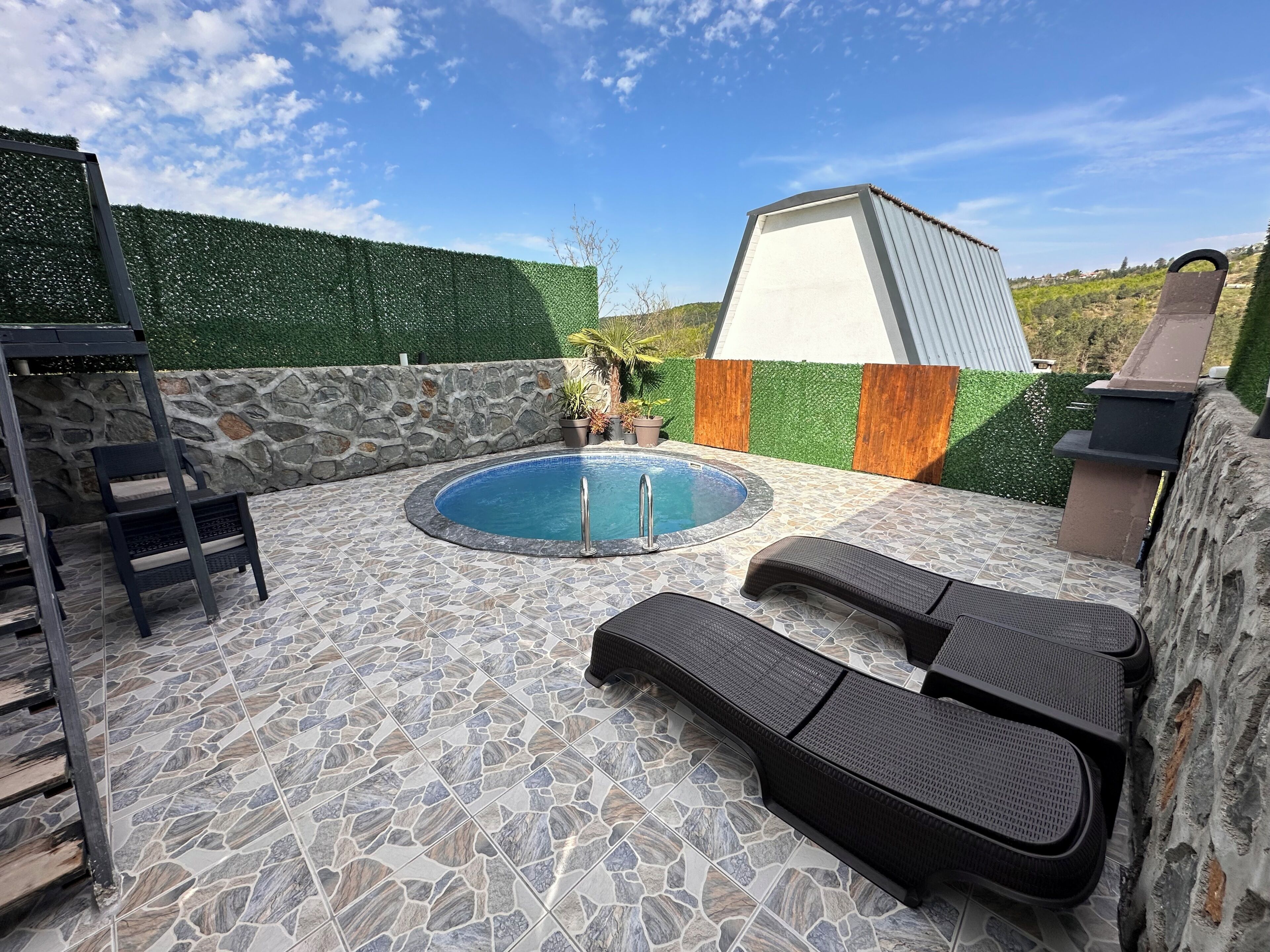 A pool area with stone tiles, lounge chairs, and a stone wall.