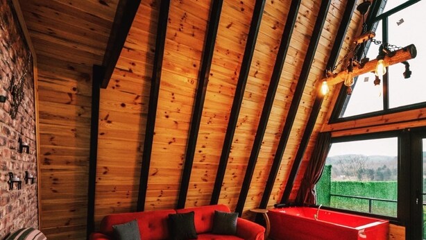 Een loft-achtige kamer met een schuine plafond, een rode bank, een houten salontafel en uitzicht op de omgeving.