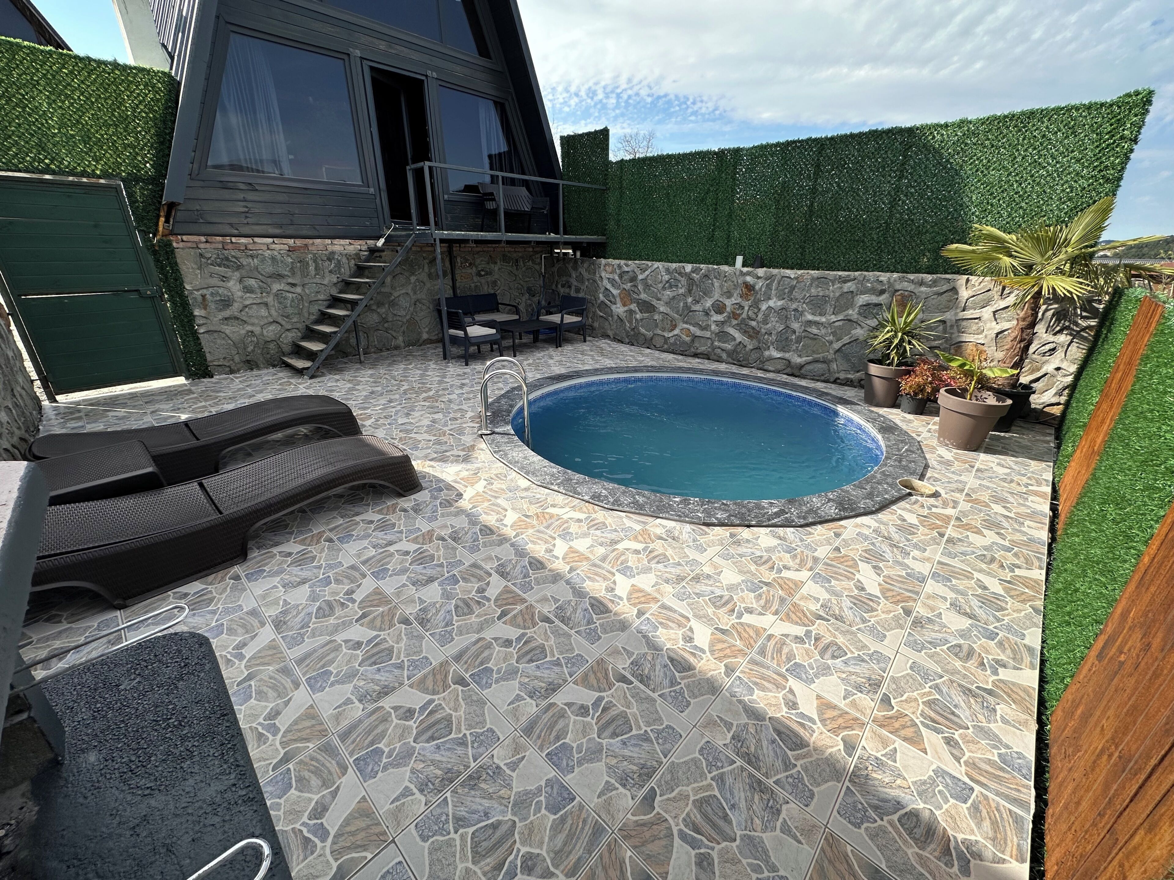 Une piscine avec des carreaux de pierre, des chaises longues et un mur en pierre.
