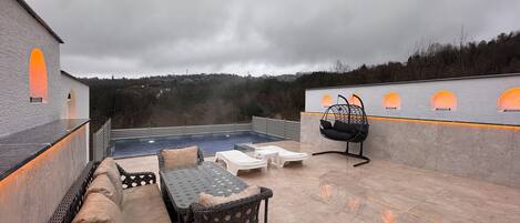 Un patio exterior con mobiliario de mimbre, una piscina y vistas del paisaje circundante.