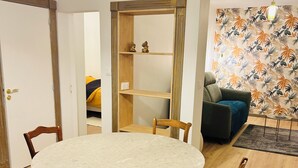 A dining area with a round table, wooden chairs, a built-in shelf unit, and a patterned wall. - Luxury apartment with parking, river and forest views, 5 min. from the center! (La Châtre)