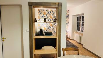 A room with a wooden shelf unit, a round table, and a view into another room with a window.