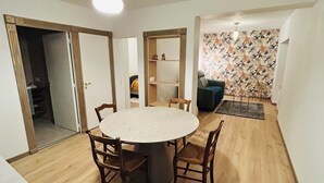 A dining area with a round table and chairs, a wooden floor, and a patterned wall. - Luxury apartment with parking, river and forest views, 5 min. from the center! (La Châtre)