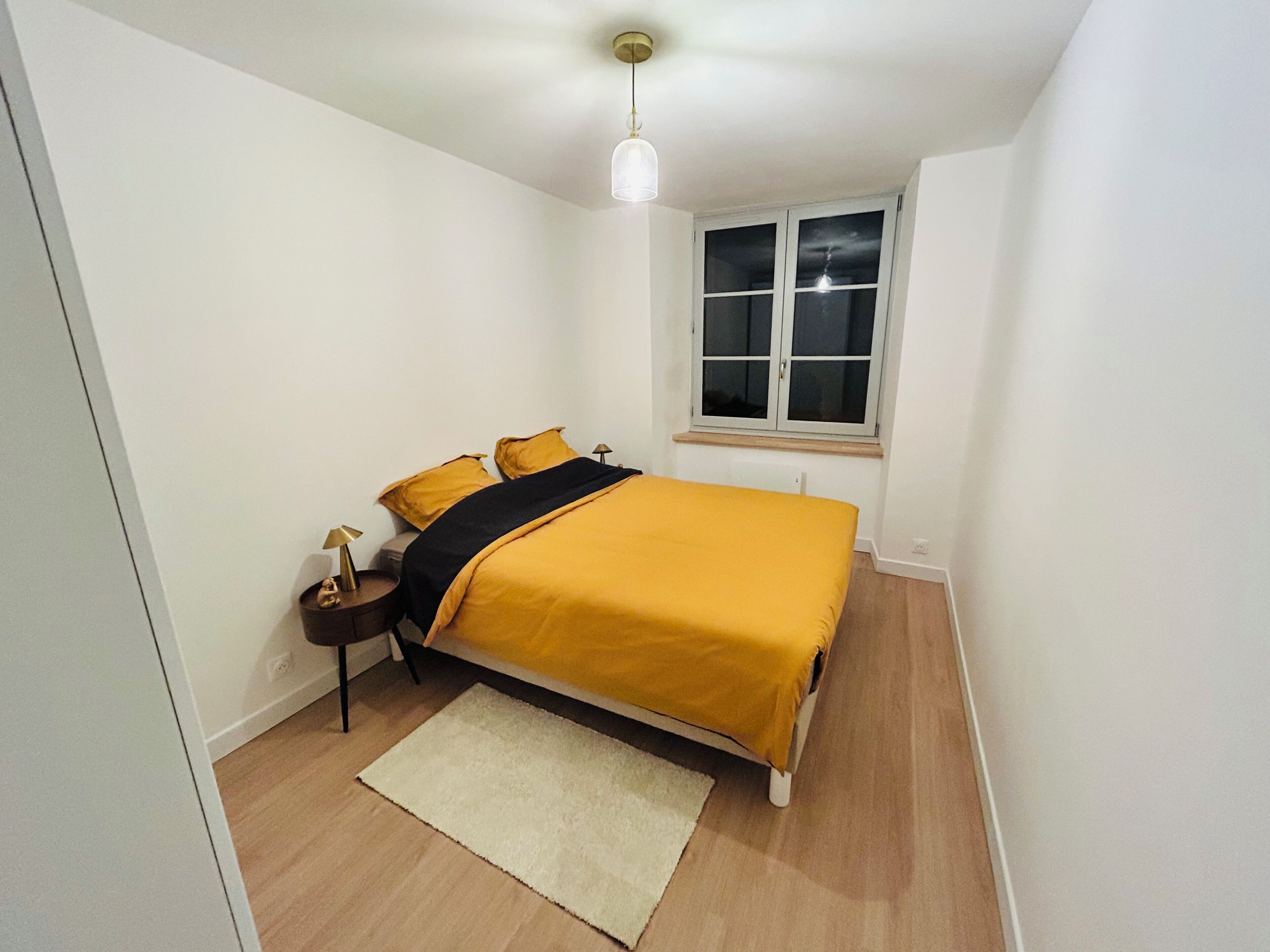 Una camera da letto con un letto, un comodino, una lampada, una finestra e una luce a soffitto.